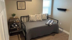 A bedroom with a bed, a bedside table, a window, and a wall-mounted shelf. - Stylish and cozy 2 bed (Brighton)