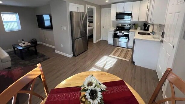 A modern kitchen with white cabinets, stainless steel appliances, and a dining area with a wooden table and chairs.