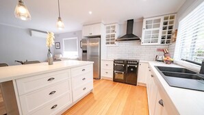 A modern kitchen with white cabinetry, a stainless steel refrigerator, a built-in oven, and a black stovetop. - 4 Bedroom fun house - spa, sauna, fire pits, pool table, 4 TV's, 2 outdoor areas (Healesville)