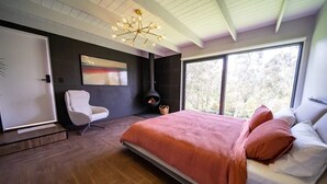 A modern bedroom with a large bed, a white chair, a fireplace, and a large window. - 4 Bedroom fun house - spa, sauna, fire pits, pool table, 4 TV's, 2 outdoor areas (Healesville)