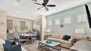 A spacious living room with a beige sofa, a glass coffee table, and a dining area with a table and chairs.
