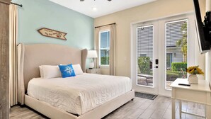 A bedroom with a large bed, a ceiling fan, a nightstand with a lamp, and a view of the outdoors through a sliding glass door.