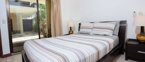 Een hotelkamer met een bed, twee bedlampen, een schuifdeur naar een balkon en een kleine tafel met een lamp.