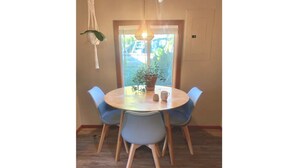 Een ronde eettafel met vier blauwe stoelen, een hangende macramé lamp en een potplant op de tafel.