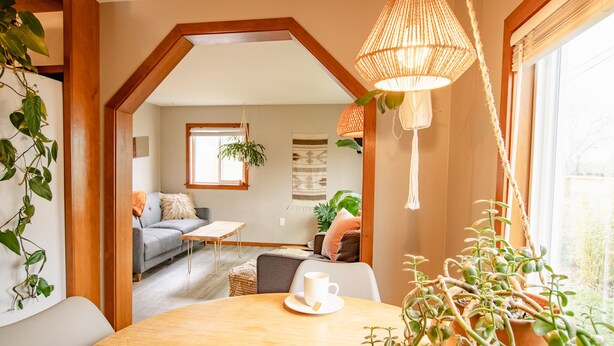 Een gezellige woonkamer met een houten plafond, een ronde houten tafel met een witte kop, en een bloempot met een plant.