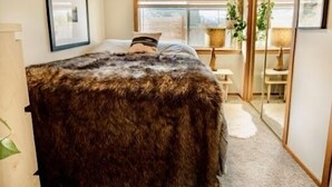 Een slaapkamer met een groot bed, een raam, een plant en een spiegel.