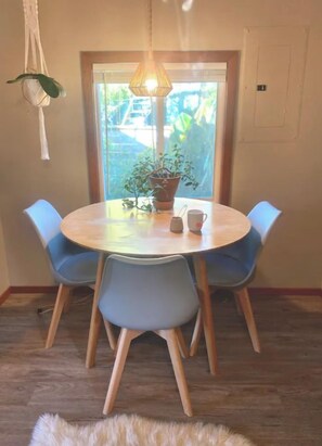 Une table de salle à manger ronde, entourée de quatre chaises bleues, un luminaire suspendu en macramé et une plante en pot posée sur la table.