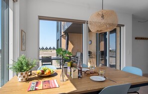 A dining area with a wooden table, chairs, a woven light fixture, and a view of a wooden deck and houses outside. - Stunning apartment in Slagelse (Slagelse)