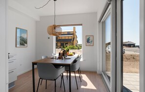 A modern dining area with a wooden table, grey chairs, and a woven pendant light. A framed map of Denmark is on the wall, and a window offers a view of a building and a car outside. - Stunning apartment in Slagelse (Slagelse)