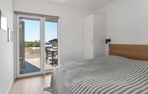 A bedroom with a bed, a sliding glass door leading to an outdoor area with a table and chairs, and a view of a car and greenery outside. - Stunning apartment in Slagelse (Slagelse)