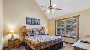 A bedroom with a bed, two nightstands, a ceiling fan, a window with blinds, and a painting on the wall.