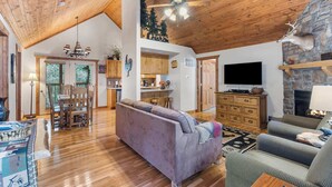 A spacious living room with a high ceiling, wooden floors, a fireplace, a television, and a dining area with a table and chairs.