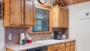 A kitchen with wooden cabinets, a double sink, a dishwasher, and a window with blinds.