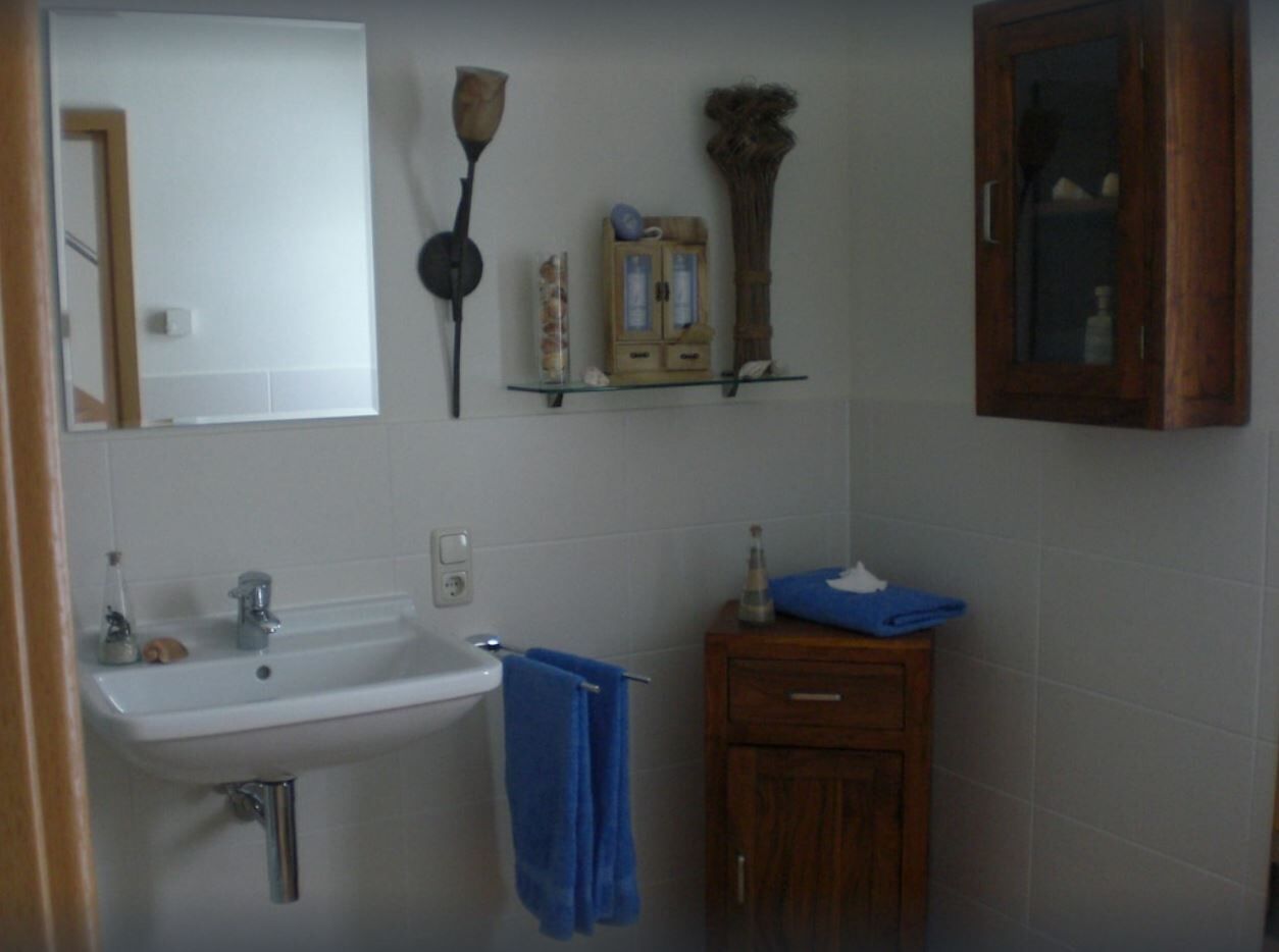 Un baño con lavamanos blanco, mueble de madera y espejo.