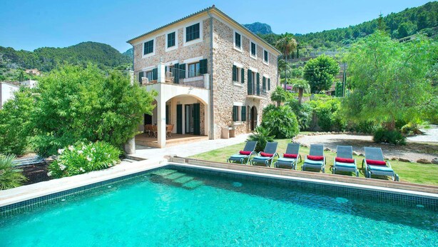 A two-story stone building with a swimming pool and sun loungers.