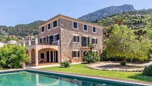 A stone building with a pool, surrounded by greenery and hills.
