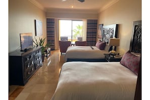 Relax in a stylish room with two beds, a flat-screen TV, and a large window offering a view of palm trees.