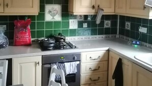 A kitchen with light wooden cabinets, a green tiled backsplash, a gas stove, and a small refrigerator.