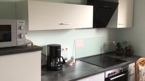 Een compacte keuken met witte kastjes, een zwarte kookplaat, een magnetron en een koffiezetapparaat.