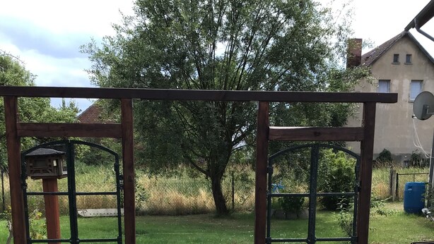 Een houten pergola met een vogelhuisje en bloempotten.