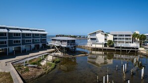 A waterfront property with multiple buildings, including a large white building with balconies and a smaller structure with a covered deck. - Corner View at Cedar Cove! Gulf View Downtown! (Cedar Key)