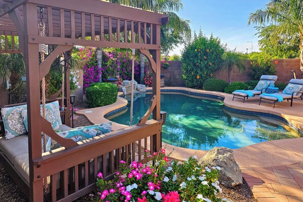Relax in a serene outdoor setting with a pergola, seating area, and pool surrounded by a beautiful garden.