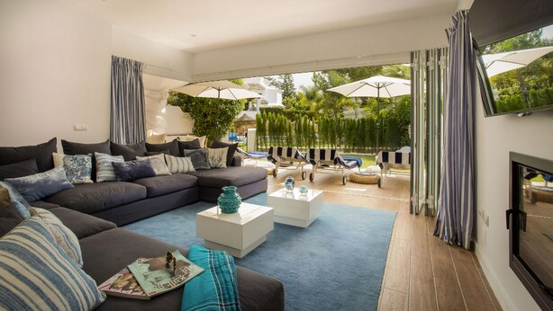 Een moderne woonkamer met een hoekbank, twee salontafels en een open haard.