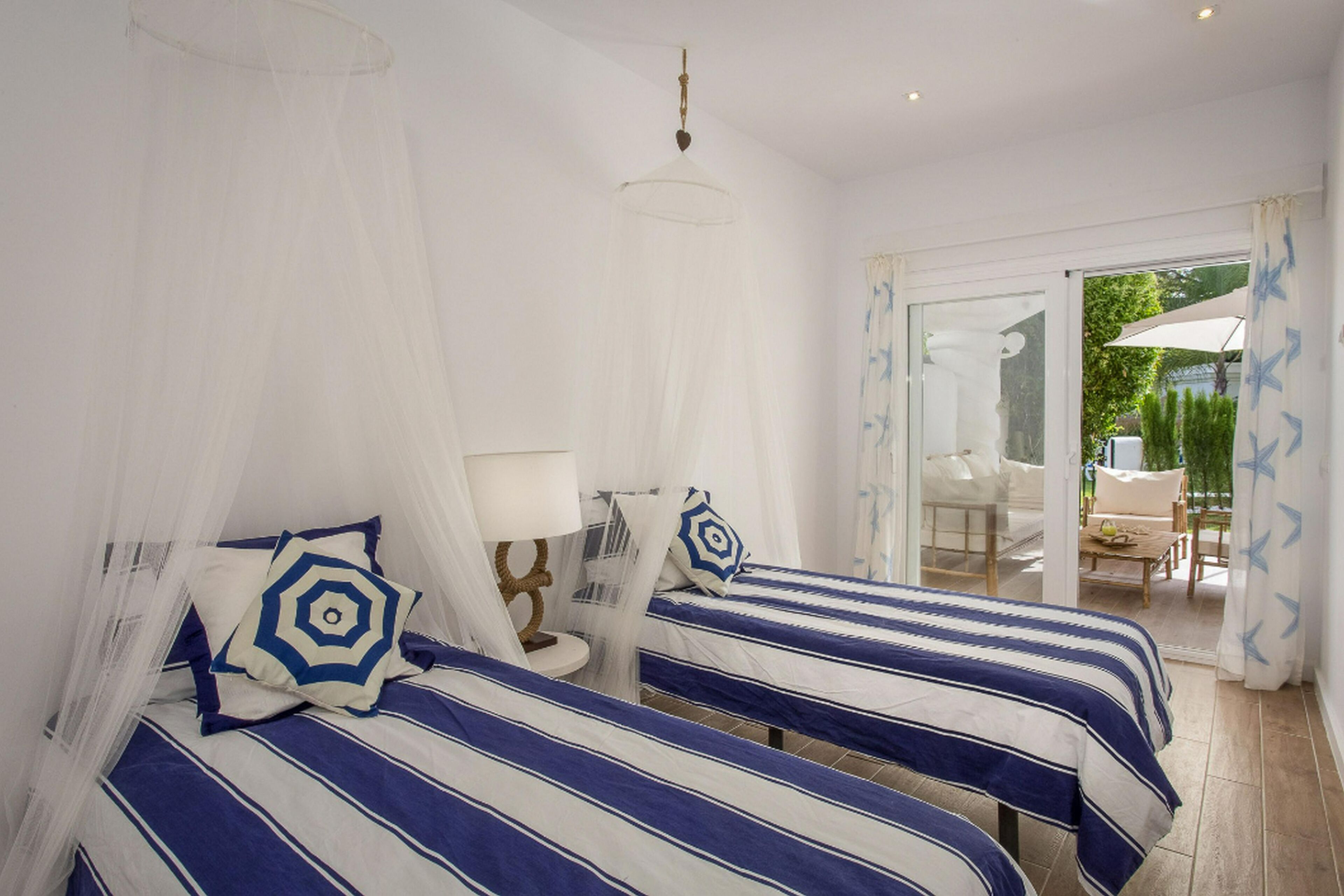 Ein Zimmer mit zwei Betten, beide mit Baldachin und gestreifter Bettwäsche. Ein Stuhl und ein Tisch befinden sich in der Nähe des Fensters.