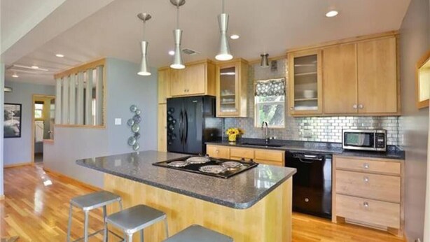 A modern kitchen with wooden cabinets, a central island with stools, stainless steel appliances, and pendant lighting.