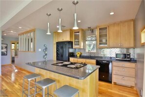 A modern kitchen with wooden cabinets, a central island with stools, stainless steel appliances, and pendant lighting. - The Loft at Stardust Mid-Century Retreat (Coleman)