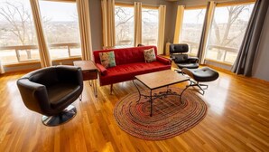 A spacious living room with a red sofa, black armchairs, a coffee table, and a large window with curtains.