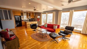 A spacious living area with a wooden floor, a red sofa, black chairs, a coffee table, and a kitchen in the background.