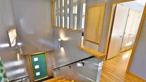 A staircase with a wooden handrail, a green door, and a mirror reflecting a hallway with doors.
