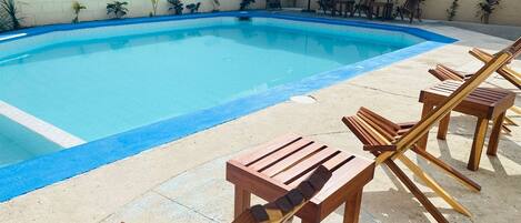 A swimming pool with wooden lounge chairs and umbrellas.