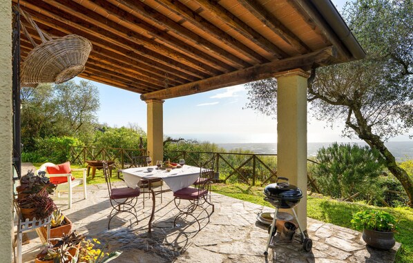 An outdoor patio with a table set for dining, surrounded by stone flooring and metal chairs.