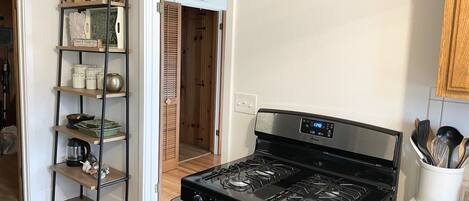 Una cocina con estufa negra, estantes de madera y un reloj en la pared.