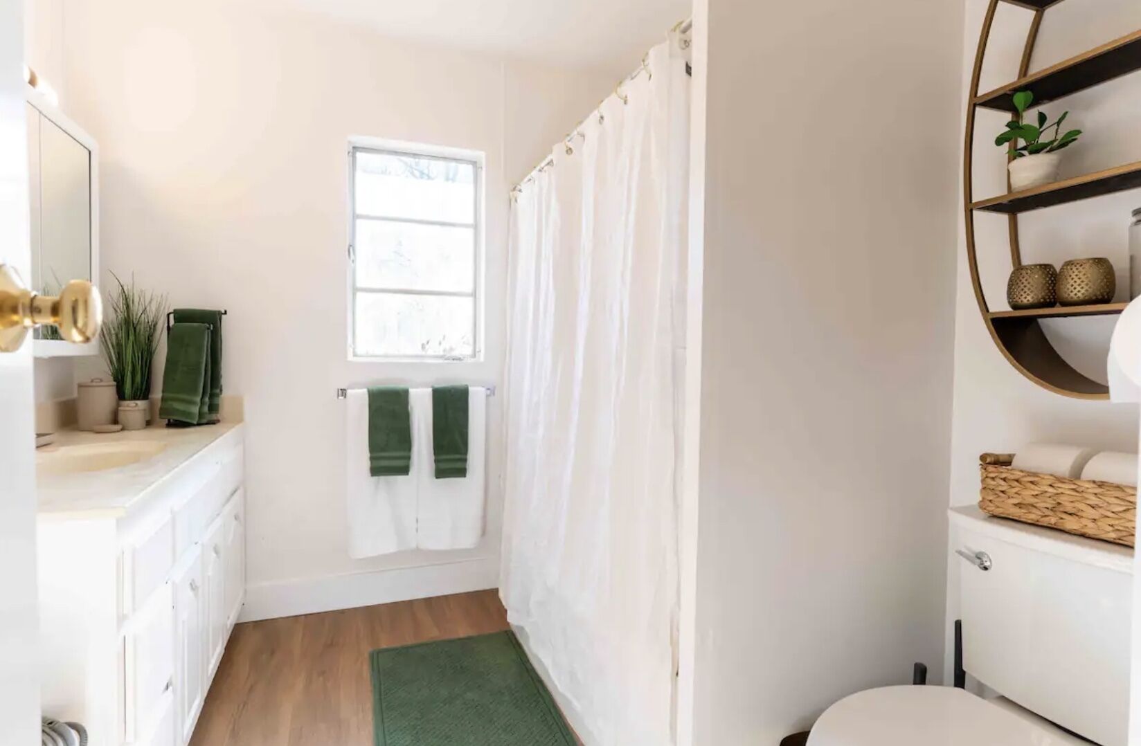 A bathroom with a white vanity, a green towel, a window, and a shower curtain.