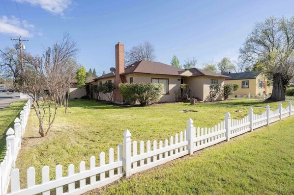 A two-story house with a brick chimney, a white picket fence, and a well-maintained lawn.