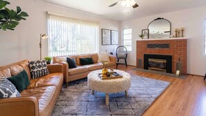 A living room with a leather sofa, a round ottoman, a fireplace, and a ceiling fan.