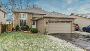 A two-story house with a brick facade, a garage, and a front yard with grass and small trees.