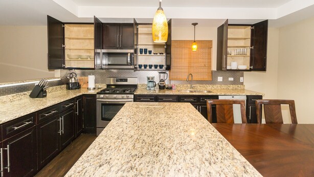 A modern kitchen with dark cabinetry, granite countertops, stainless steel appliances, and a central island.