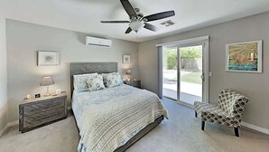 A bedroom with a bed, a nightstand, a chair, a ceiling fan, and a sliding glass door leading to a patio. - Luxe Retreat - Backyard Oasis (Palm Springs)