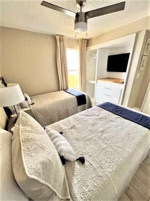 A hotel room with a bed, a desk, a chair, a lamp, a ceiling fan, and a TV.