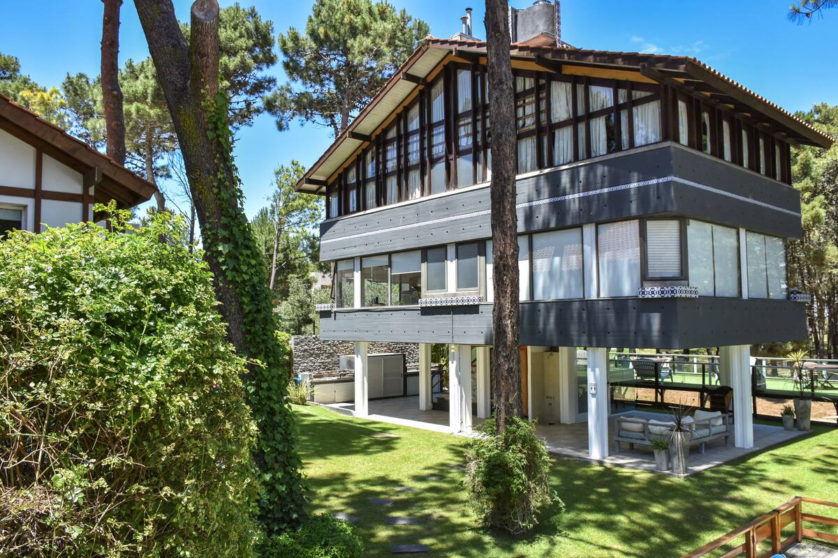 Una casa de dos plantas con balcón, rodeada de árboles y un césped cuidado.