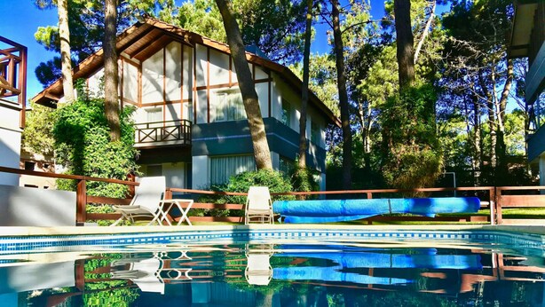 Una piscina amb una terrassa de fusta, gandules i un edifici amb un balcó.
