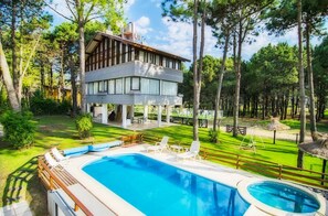 A two-story house with a swimming pool, surrounded by a well-maintained lawn and trees. - suites del bosque (Pinamar)