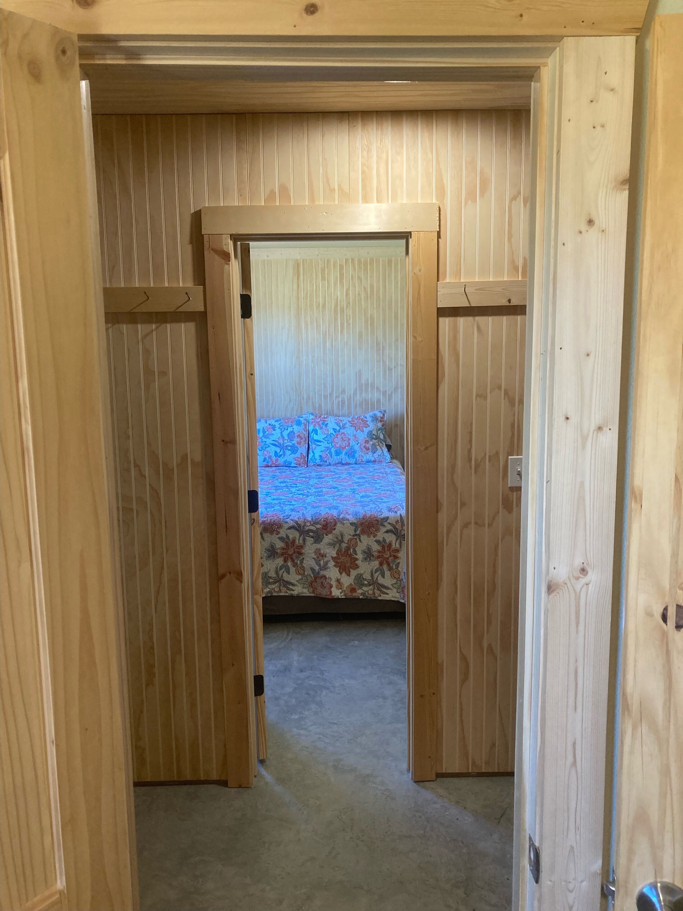 A wooden-paneled room with a bed at the end of a narrow hallway.