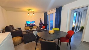 Uma sala de estar moderna com área de jantar, televisão, árvore de Natal e varanda com portas de vidro.