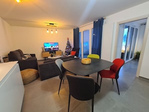 A modern living room with a dining area, a television, a Christmas tree, and a balcony with glass doors.