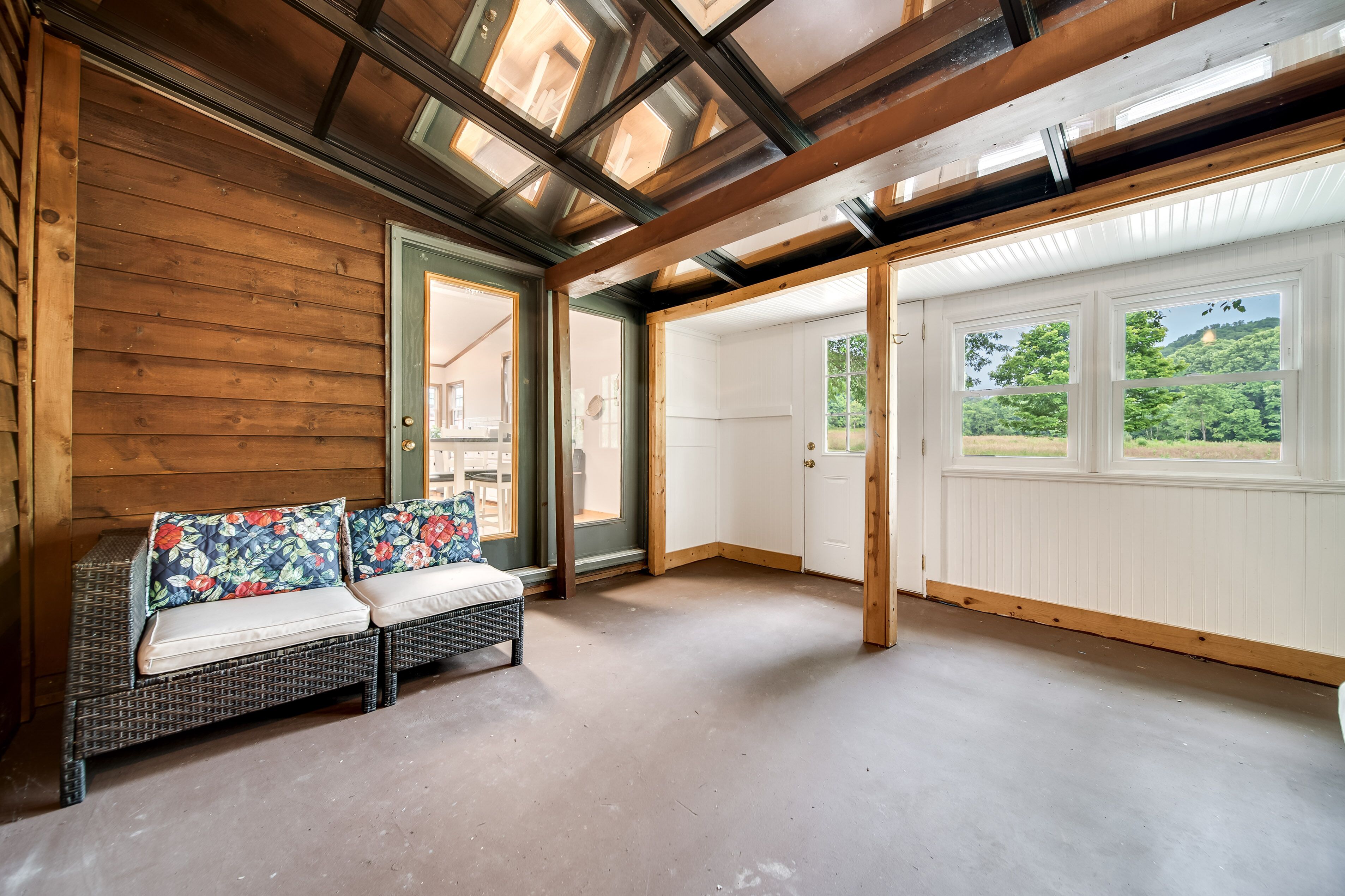 A room with a wooden bench, a door leading outside, and a view of greenery through large windows.